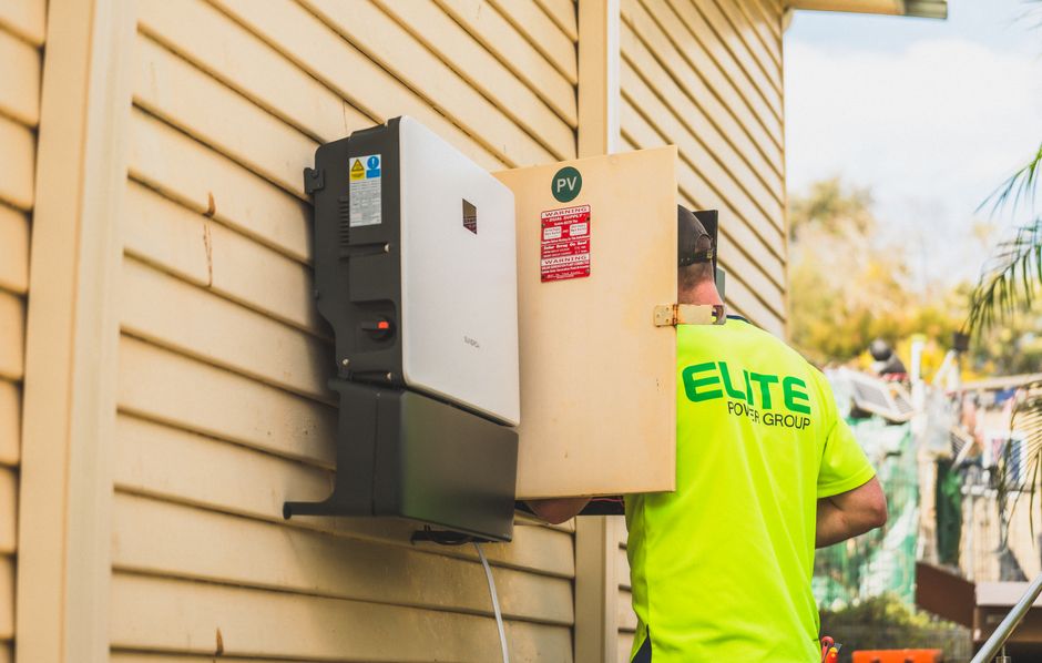 Electrician from Elite Power Group installing a solar inverter outside.