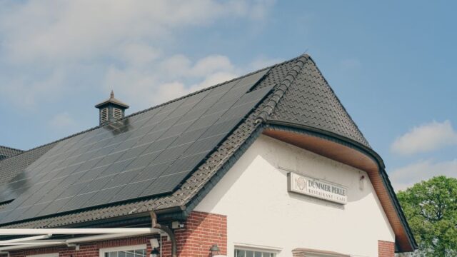A red brick building with solar panels on the roof, under a clear blue sky, symbolizing sustainability and renewable energy.