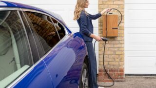 A woman efficiently charges her blue electric car at a home EV charging station.
