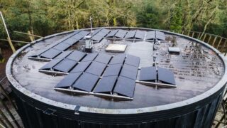 Aerial view of a round rooftop with solar panels surrounded by trees, promoting renewable energy.