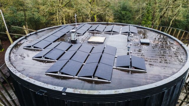Aerial view of a round rooftop with solar panels surrounded by trees, promoting renewable energy.