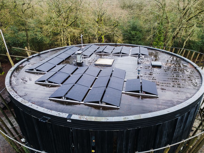 Aerial view of a round rooftop with solar panels surrounded by trees, promoting renewable energy.