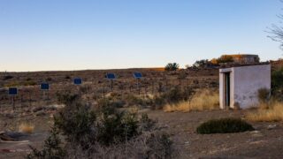 Solar panels in a desert landscape with a shed under a clear sunset sky.