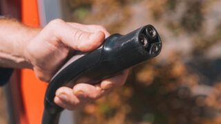 Hand holding an electric vehicle charging plug, symbolizing clean energy and innovation.