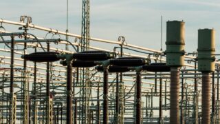 Detailed view of electrical substation with high voltage equipment and insulators against a clear sky.