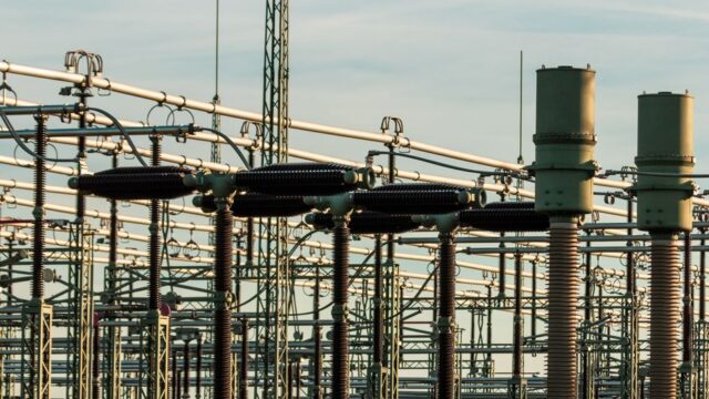 Detailed view of electrical substation with high voltage equipment and insulators against a clear sky.