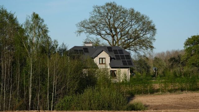 Modern house with solar panels surrounded by lush trees and fields, embracing sustainable living.