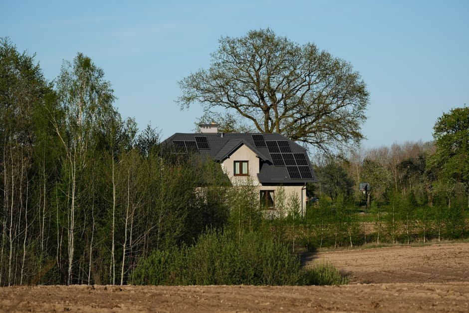 Modern house with solar panels surrounded by lush trees and fields, embracing sustainable living.
