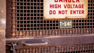 Close-up of a rusty industrial gate with a high voltage warning sign, conveying danger.