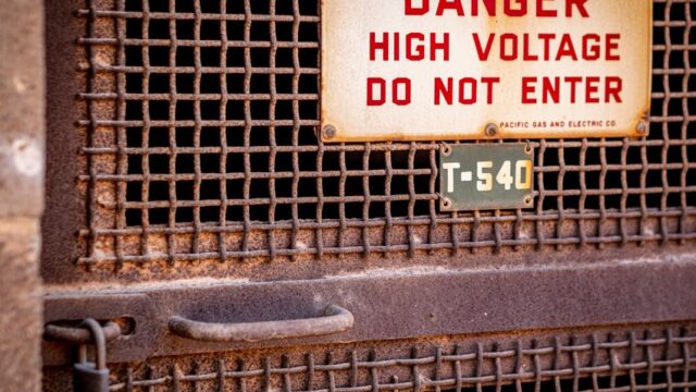 Close-up of a rusty industrial gate with a high voltage warning sign, conveying danger.