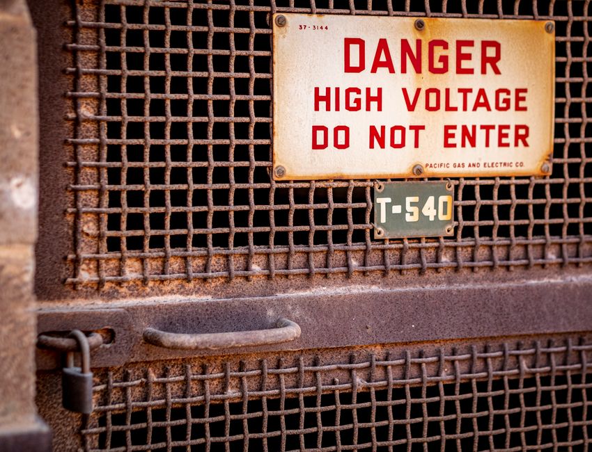 Close-up of a rusty industrial gate with a high voltage warning sign, conveying danger.