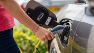 Close-up of a person plugging in an electric car at a charging station outdoors.
