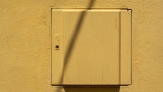 Yellow electrical panel on a textured wall under sunlight casting shadows.