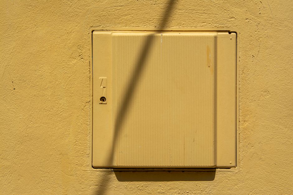 Yellow electrical panel on a textured wall under sunlight casting shadows.