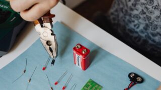 Close-up of electronics repair using pliers with resistors and battery.