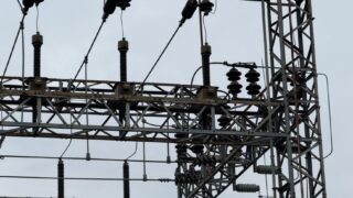 Close-up of high voltage power lines with intricate metal structures against a cloudy sky.