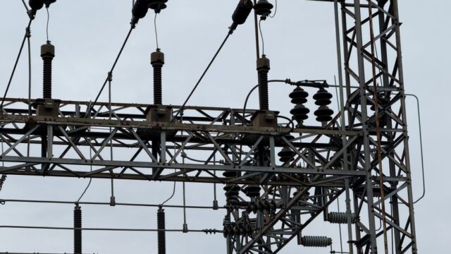 Close-up of high voltage power lines with intricate metal structures against a cloudy sky.