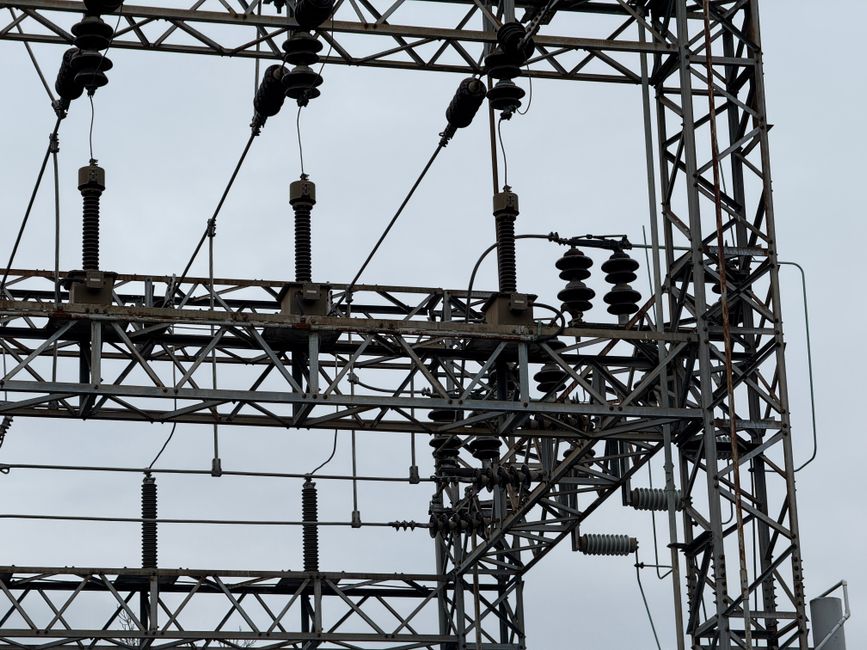 Close-up of high voltage power lines with intricate metal structures against a cloudy sky.