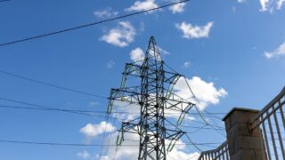 High voltage transmission tower against a clear blue sky with clouds.