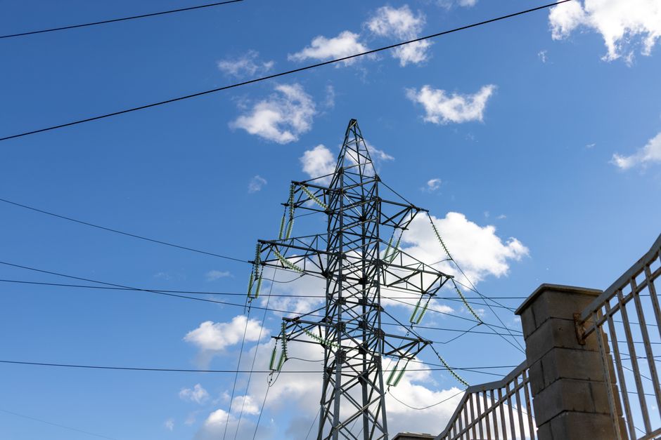 High voltage transmission tower against a clear blue sky with clouds.