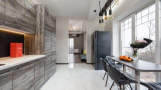 Table with fruits and flowers placed near window near counter and gray cupboards in stylish kitchen with fridge in apartment