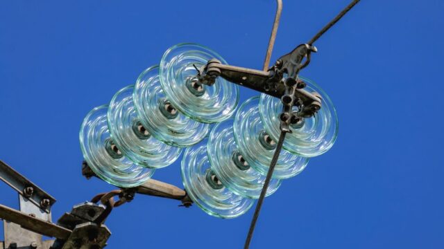 Close-up of a high voltage glass insulator suspended against a bright blue sky, reflecting modern electrical technology.