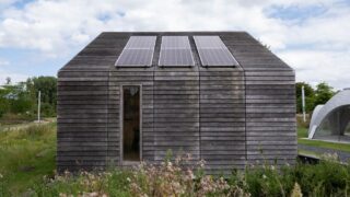 Sustainable wooden house with solar panels and lush surroundings.