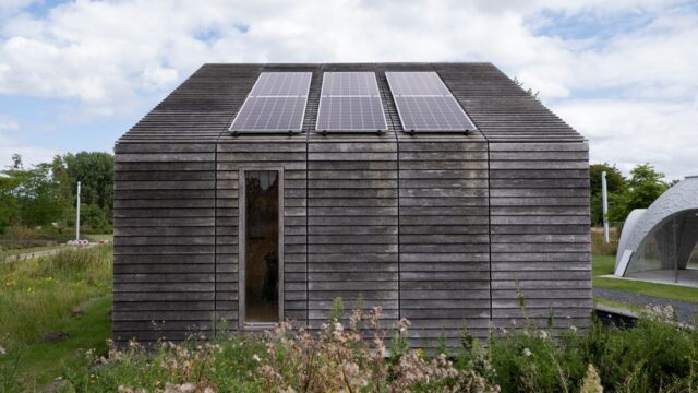 Sustainable wooden house with solar panels and lush surroundings.