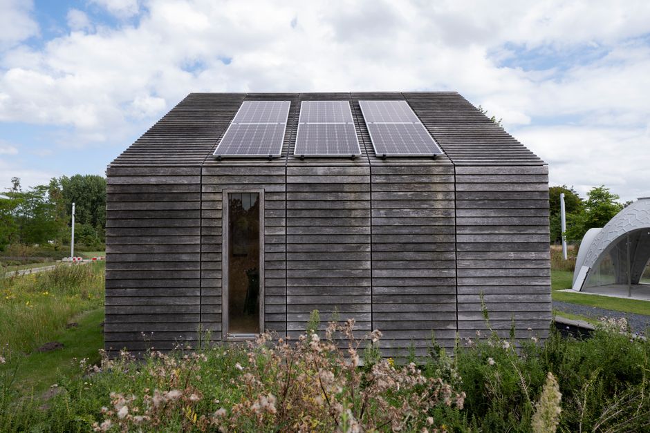 Sustainable wooden house with solar panels and lush surroundings.