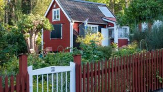 Picturesque red cottage with lush garden, solar panels, and Swedish flag in Stockholm.
