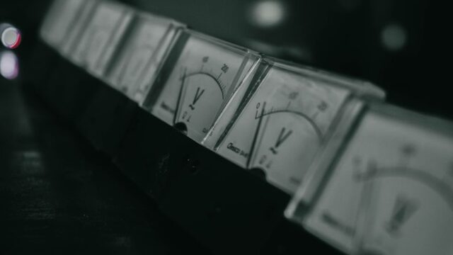 Close-up of vintage analog voltage meters in a dark industrial setting with a moody atmosphere.
