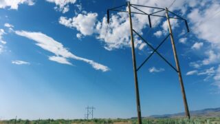 Scenic view of high voltage power lines in a field with a bright blue sky and fluffy clouds.