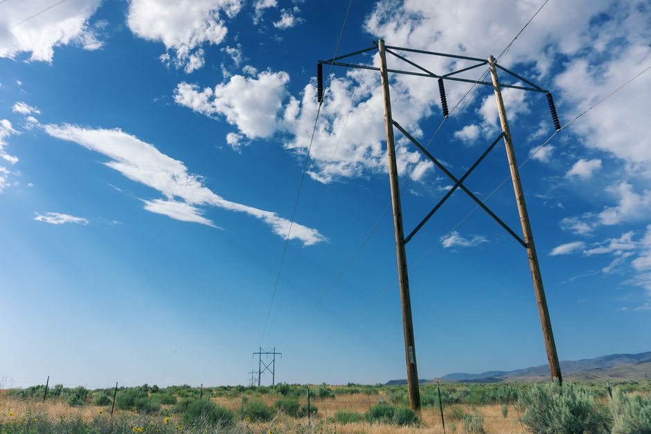 Scenic view of high voltage power lines in a field with a bright blue sky and fluffy clouds.
