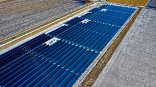 Aerial shot of expansive solar panel installation in snowy fields during daylight in Claremont, MN.