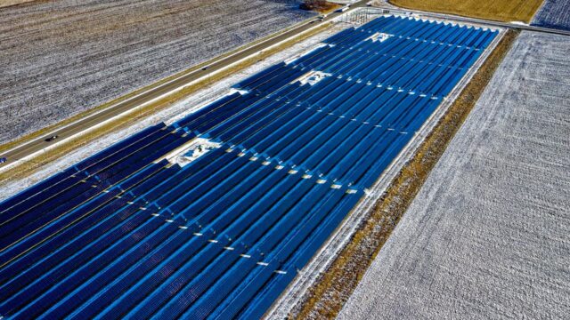 Aerial shot of expansive solar panel installation in snowy fields during daylight in Claremont, MN.