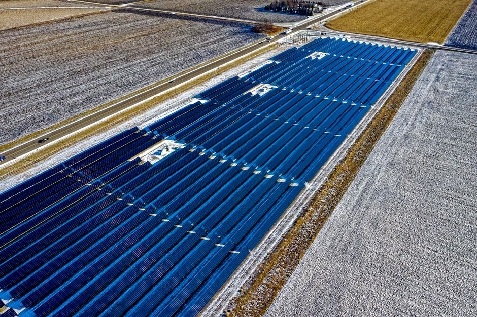 Aerial shot of expansive solar panel installation in snowy fields during daylight in Claremont, MN.