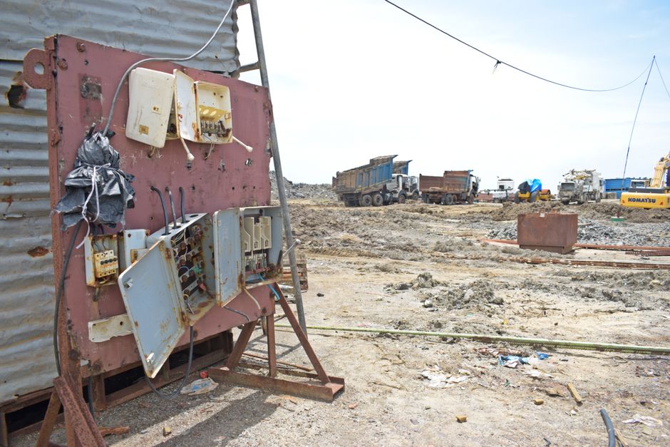 A barren construction site with rusted electrical panel and heavy equipment in the background.