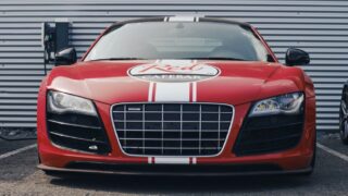 Bold red sports car parked in front of a charging station with a distinctive grille and emblem.