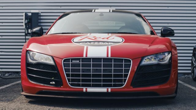 Bold red sports car parked in front of a charging station with a distinctive grille and emblem.