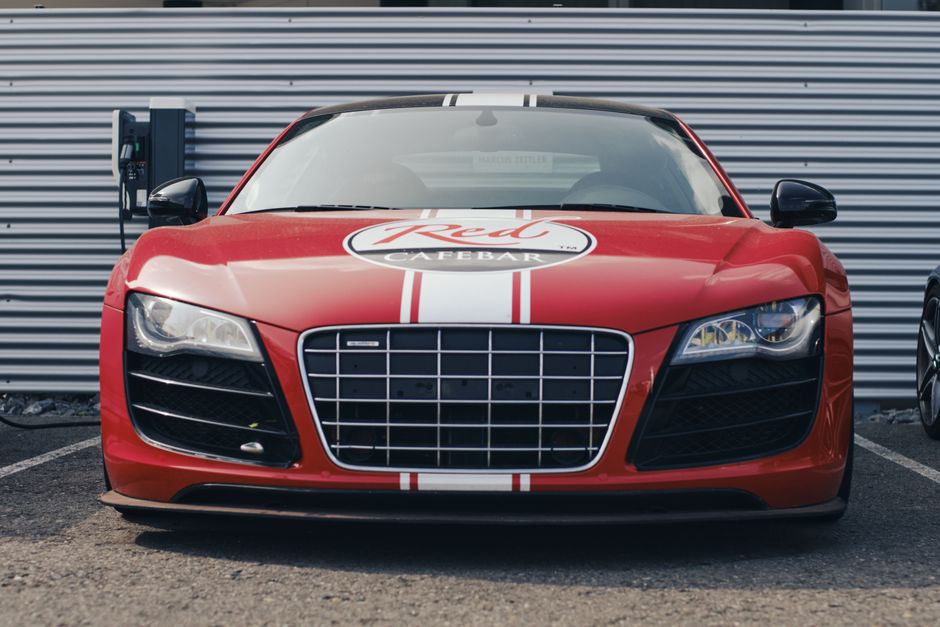 Bold red sports car parked in front of a charging station with a distinctive grille and emblem.