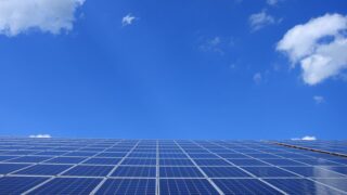 A low angle view of solar panels under a bright blue sky with clouds.
