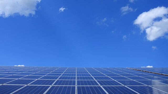 A low angle view of solar panels under a bright blue sky with clouds.