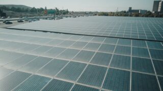 Rows of solar panels near a highway capture renewable energy under a clear sky.