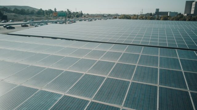 Rows of solar panels near a highway capture renewable energy under a clear sky.