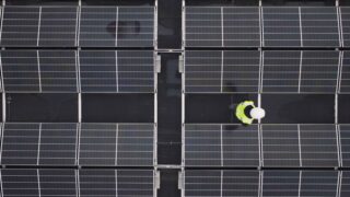Aerial view of a worker inspecting solar panels on a rooftop, promoting renewable energy.