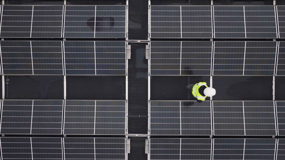 Aerial view of a worker inspecting solar panels on a rooftop, promoting renewable energy.