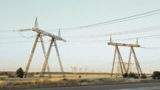 Wide-angle view of high voltage power lines crossing a rural field under a clear sky.