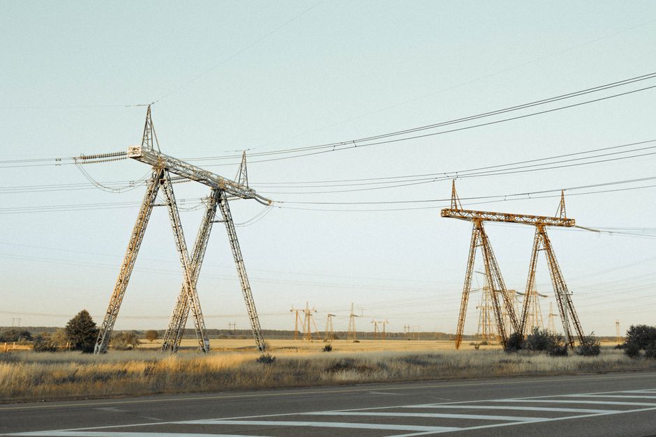 Wide-angle view of high voltage power lines crossing a rural field under a clear sky.