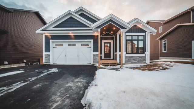 Exterior of modern blue cottage house surrounded by residential houses and snow in daylight
