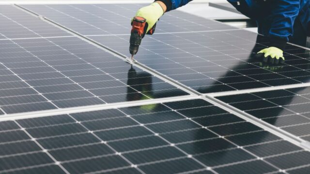 A technician uses a power tool to install solar panels, showcasing renewable energy efforts.